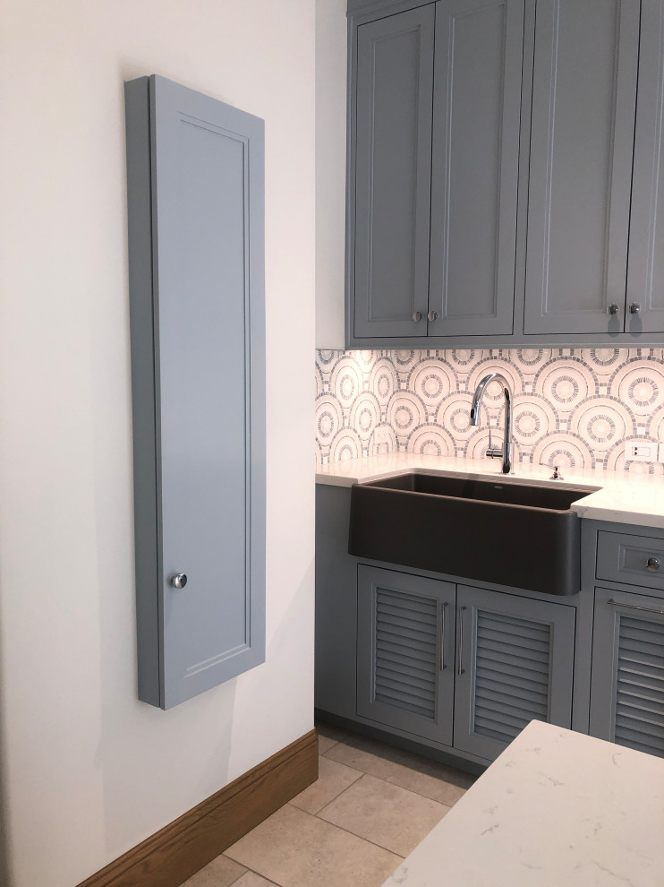 Inspiration for a large transitional u-shaped dedicated laundry room in San Diego with a farmhouse sink, shaker cabinets, blue cabinets, quartz benchtops, blue splashback, mosaic tile splashback, white walls, porcelain floors, a side-by-side washer and dryer, grey floor and white benchtop.