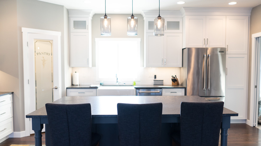Example of a large transitional u-shaped eat-in kitchen design with a farmhouse sink, flat-panel cabinets, white cabinets, granite countertops, white backsplash, ceramic backsplash, stainless steel appliances and an island