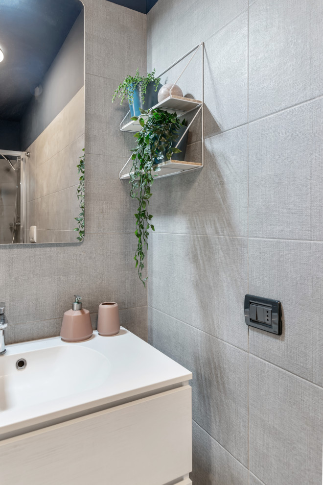 This is an example of a mid-sized tropical powder room in Milan with white cabinets, a two-piece toilet, gray tile, porcelain tile, blue walls, medium hardwood floors, a drop-in sink, grey floor and white benchtops.
