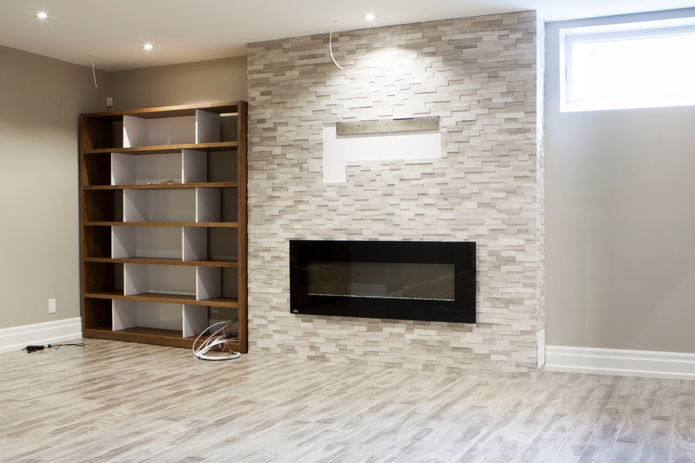 Photo of a large modern fully buried basement in Toronto with grey walls, laminate floors, a standard fireplace, a brick fireplace surround and grey floor.