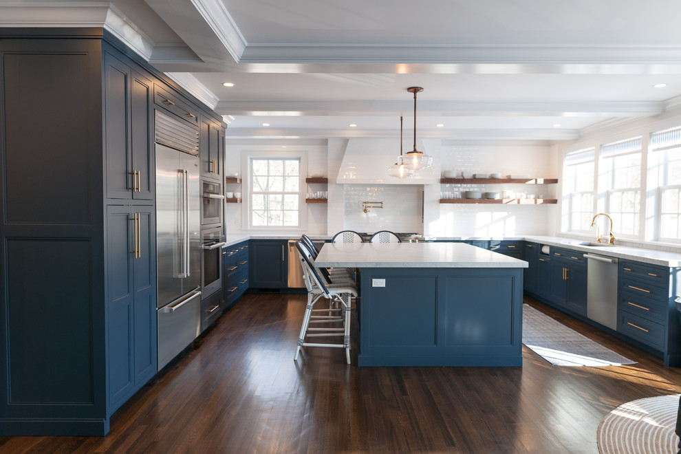 Photo of a large country u-shaped eat-in kitchen in New York with an undermount sink, shaker cabinets, blue cabinets, quartz benchtops, white splashback, subway tile splashback, stainless steel appliances, dark hardwood floors, with island, brown floor and white benchtop.