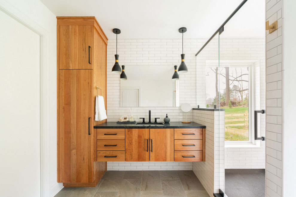 This is an example of a contemporary master bathroom in Philadelphia with flat-panel cabinets, white tile, white walls, soapstone benchtops, a hinged shower door, black benchtops, a floating vanity and subway tile.