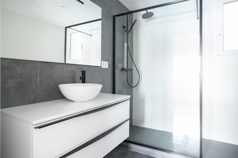 This is an example of a mid-sized contemporary master bathroom in Barcelona with flat-panel cabinets, white cabinets, an alcove shower, a one-piece toilet, gray tile, ceramic tile, white walls, ceramic floors, a trough sink, grey floor, a sliding shower screen, white benchtops, an enclosed toilet, a single vanity and a floating vanity.