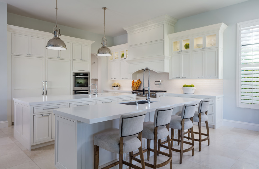 Photo of a transitional kitchen in Hawaii with an undermount sink, shaker cabinets, white cabinets, white splashback, stainless steel appliances, beige floor, white benchtop and multiple islands.