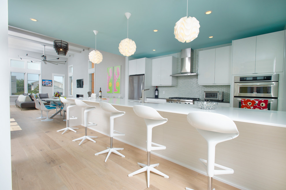 Photo of a large contemporary open plan kitchen in Wilmington with an undermount sink, flat-panel cabinets, white cabinets, blue splashback, stainless steel appliances, light hardwood floors, with island and brown floor.
