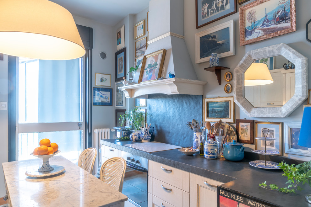 This is an example of a small eclectic single-wall separate kitchen in Venice with a drop-in sink, raised-panel cabinets, white cabinets, marble benchtops, black splashback, slate splashback, white appliances, porcelain floors, grey floor and black benchtop.