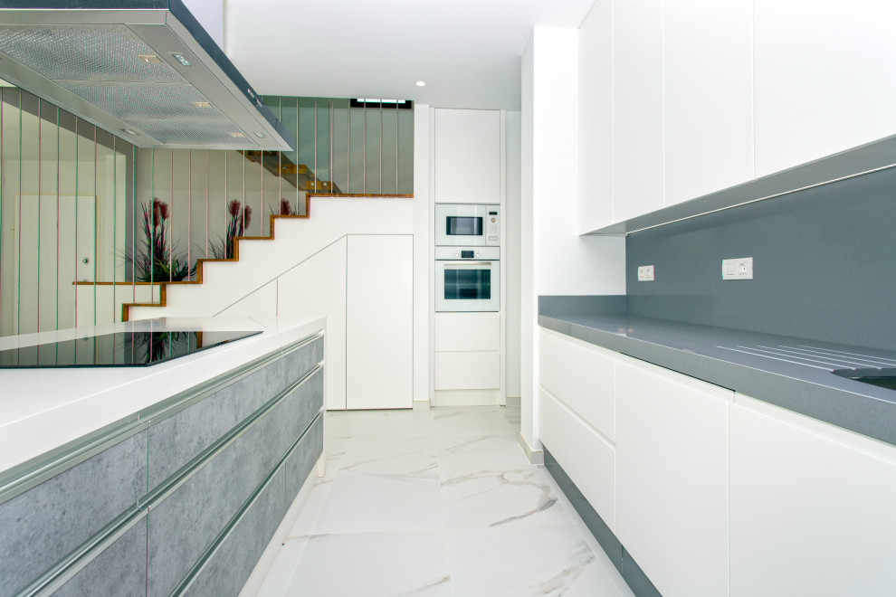 Идея дизайна: большая прямая, серо-белая кухня в современном стиле с серым фартуком, техникой под мебельный фасад, полом из керамической плитки, островом, белым полом и белой столешницей