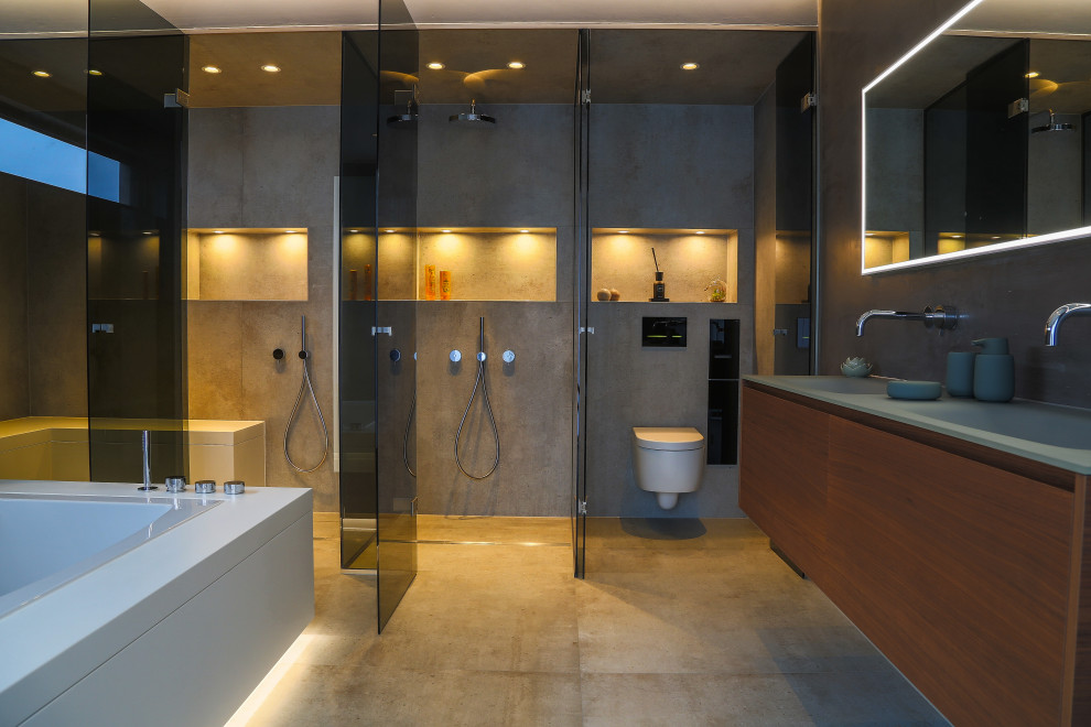 Photo of a large modern master bathroom in Frankfurt with flat-panel cabinets, dark wood cabinets, a drop-in tub, a curbless shower, a wall-mount toilet, gray tile, stone tile, grey walls, cement tiles, an integrated sink, glass benchtops, beige floor, an open shower, green benchtops, a shower seat, a double vanity, a floating vanity, recessed and decorative wall panelling.