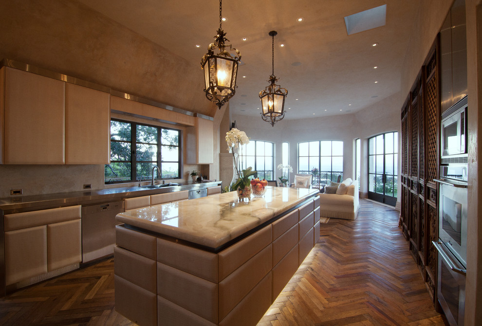 This is an example of a large traditional u-shaped open plan kitchen in Santa Barbara with an undermount sink, flat-panel cabinets, light wood cabinets, stainless steel benchtops, stainless steel appliances, medium hardwood floors, with island and brown floor.