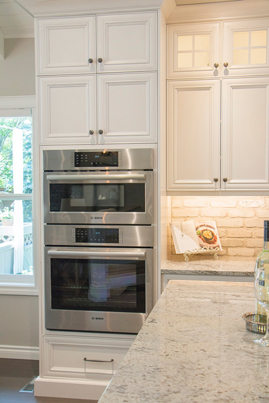 Large transitional l-shaped eat-in kitchen photo with a double-bowl sink, shaker cabinets, white cabinets, beige backsplash, stainless steel appliances and an island