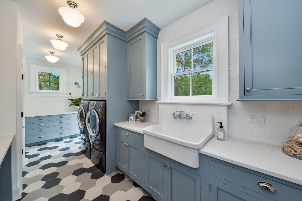 シカゴにあるラグジュアリーな広いトラディショナルスタイルのおしゃれな家事室 (エプロンフロントシンク、インセット扉のキャビネット、白いキャビネット、珪岩カウンター、白いキッチンパネル、サブウェイタイルのキッチンパネル、白い壁、セラミックタイルの床、左右配置の洗濯機・乾燥機、グレーの床、白いキッチンカウンター) の写真