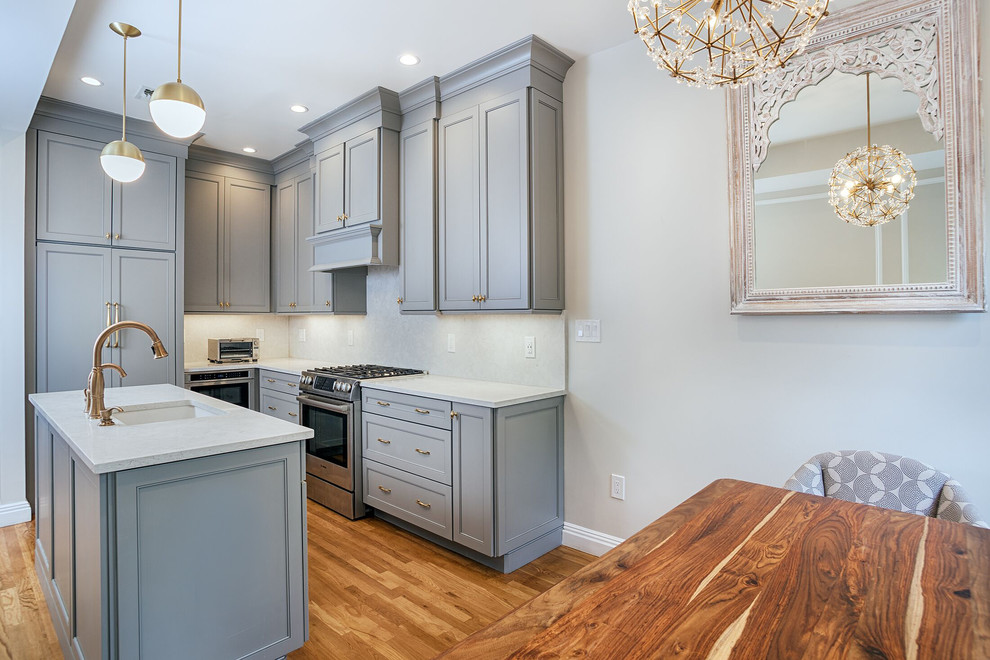 Photo of a small transitional l-shaped eat-in kitchen in New York with an undermount sink, recessed-panel cabinets, grey cabinets, quartzite benchtops, white splashback, stone slab splashback, stainless steel appliances, with island, beige floor, medium hardwood floors and white benchtop.