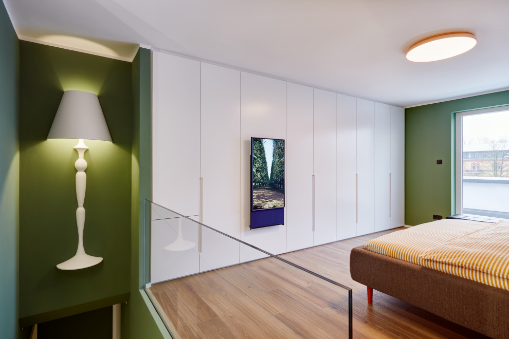 Réalisation d'une grande chambre parentale design avec un mur vert et un sol en bois brun.