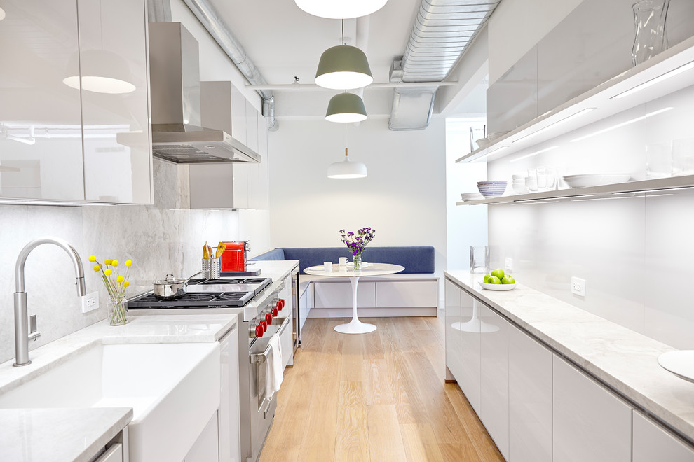 Design ideas for a contemporary galley eat-in kitchen in New York with a farmhouse sink, flat-panel cabinets, white cabinets, marble splashback, stainless steel appliances, light hardwood floors, no island, marble benchtops, white splashback and beige floor.