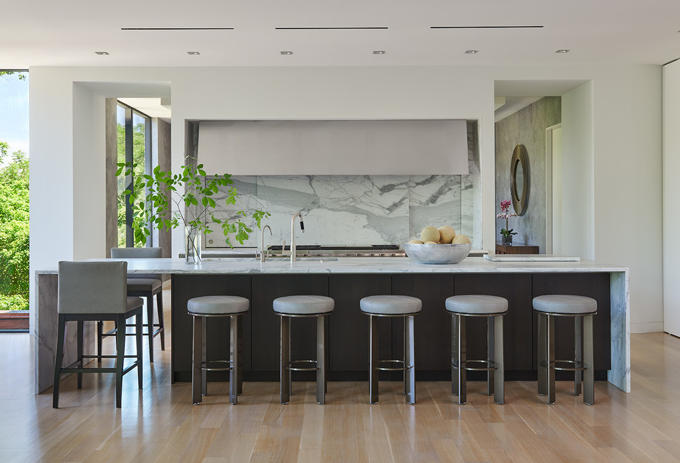 Large contemporary galley eat-in kitchen in DC Metro with an integrated sink, flat-panel cabinets, dark wood cabinets, white splashback, stone slab splashback, stainless steel appliances, medium hardwood floors, with island, brown floor, white benchtop and marble benchtops.