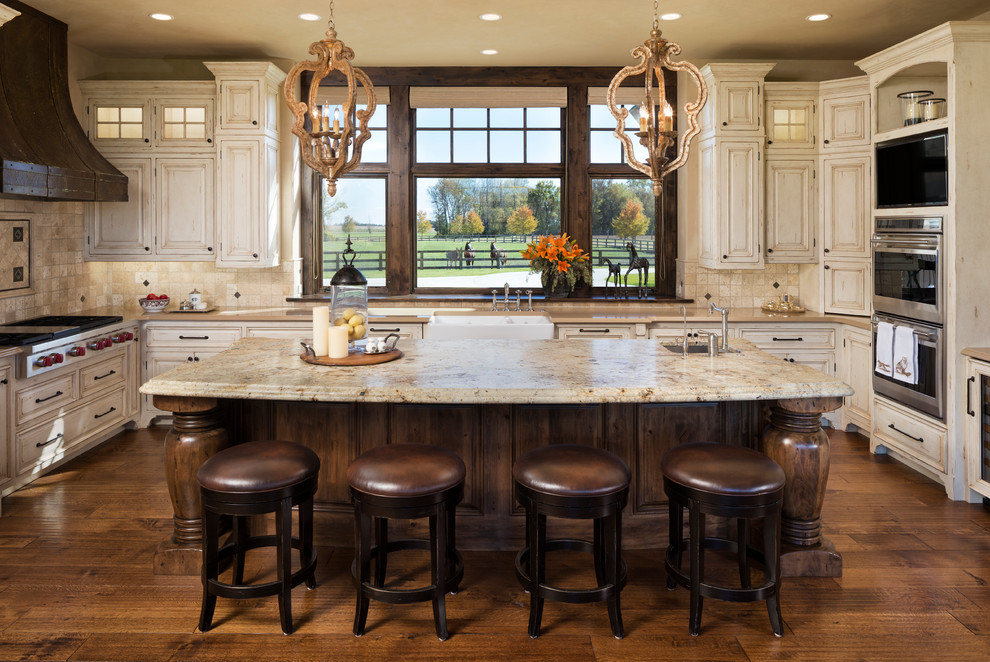 Design ideas for an expansive country u-shaped kitchen in Minneapolis with a farmhouse sink, raised-panel cabinets, distressed cabinets, granite benchtops, beige splashback, stone tile splashback, stainless steel appliances, dark hardwood floors, with island and brown floor.