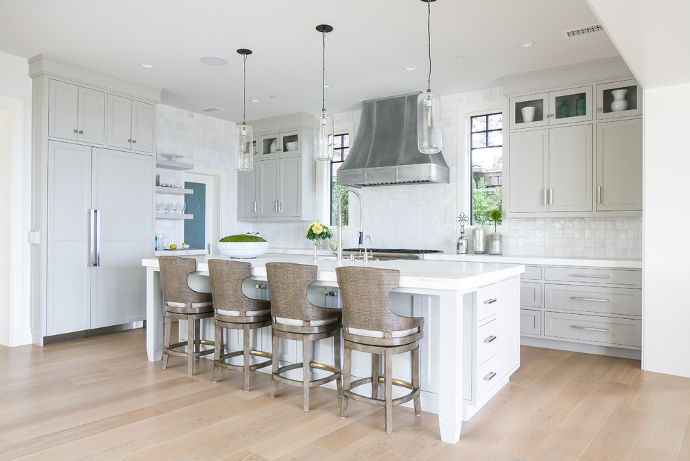 Photo of a beach style l-shaped kitchen in Orange County with shaker cabinets, grey cabinets, white splashback, panelled appliances, light hardwood floors, with island and brown floor.