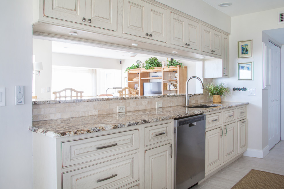 Inspiration for a mid-sized beach style galley kitchen in Miami with raised-panel cabinets, light wood cabinets, granite benchtops, beige splashback, travertine splashback, stainless steel appliances and light hardwood floors.