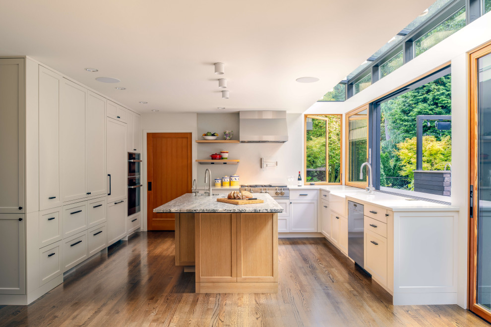 Transitional u-shaped kitchen in Seattle with a farmhouse sink, shaker cabinets, white cabinets, white splashback, stainless steel appliances, medium hardwood floors, with island, brown floor and white benchtop.