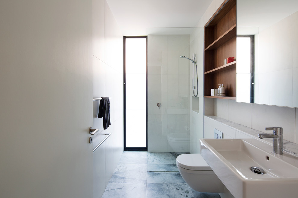 This is an example of a mid-sized contemporary bathroom in Sydney with medium wood cabinets, a wall-mount toilet, white tile, ceramic tile, white walls and marble benchtops.