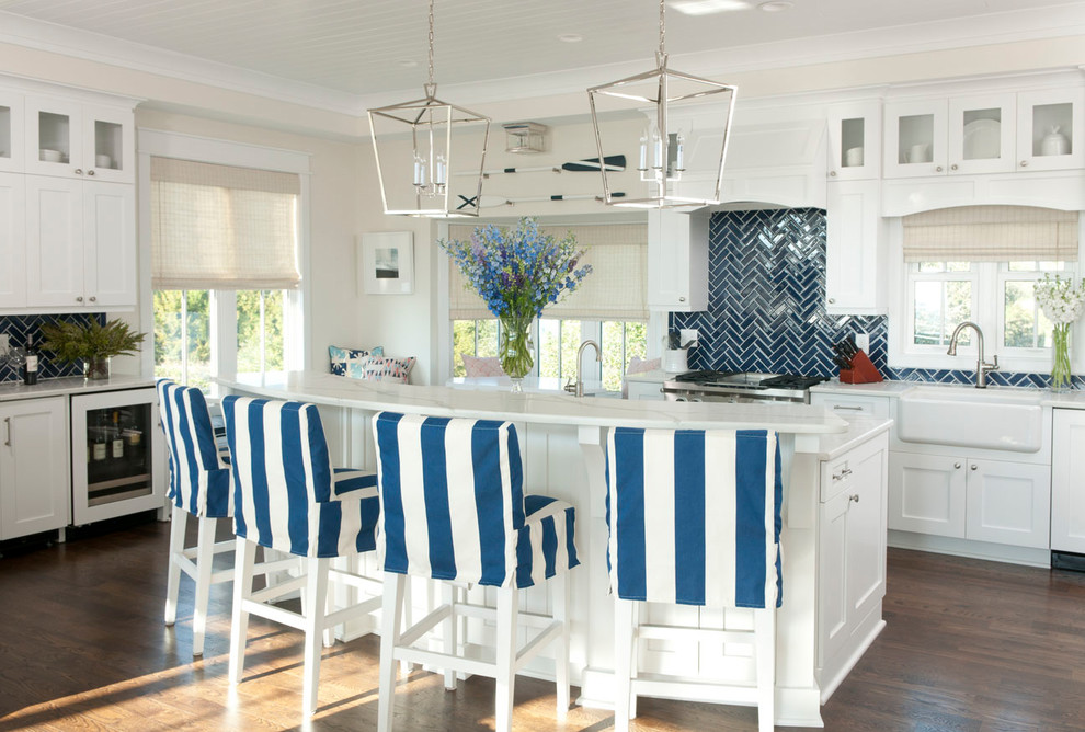 Photo of a beach style l-shaped kitchen in Other with a farmhouse sink, shaker cabinets, white cabinets, blue splashback, subway tile splashback, stainless steel appliances, medium hardwood floors, with island and brown floor.