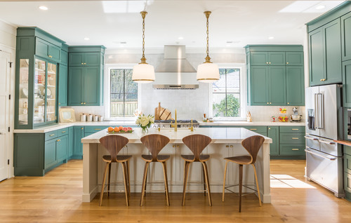 Modern kitchen with teal shaker RTA cabinets, brass hardware, white quartz island, pendant lights, stainless range hood and appliances, and warm wood floors.