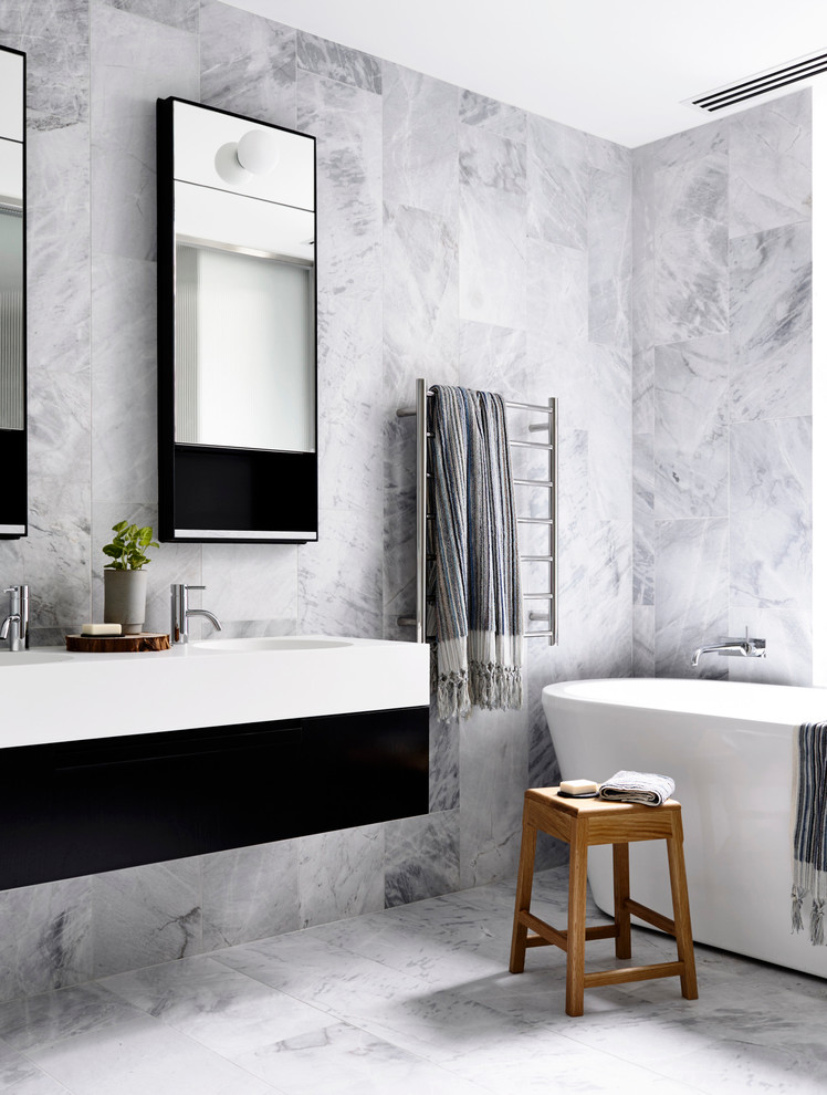 This is an example of a contemporary bathroom in New York with flat-panel cabinets, black cabinets, a freestanding tub, white tile and an integrated sink.
