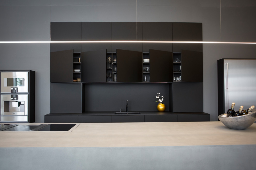 Inspiration for a modern galley open plan kitchen in Frankfurt with a drop-in sink, flat-panel cabinets, black cabinets, concrete benchtops, black splashback, stainless steel appliances, cement tiles, with island, grey floor and grey benchtop.