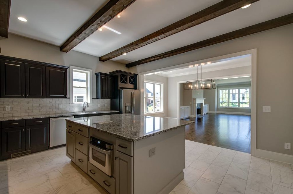 Example of a mid-sized transitional l-shaped ceramic tile and white floor open concept kitchen design with an undermount sink, raised-panel cabinets, brown cabinets, granite countertops, white backsplash, ceramic backsplash, stainless steel appliances and an island
