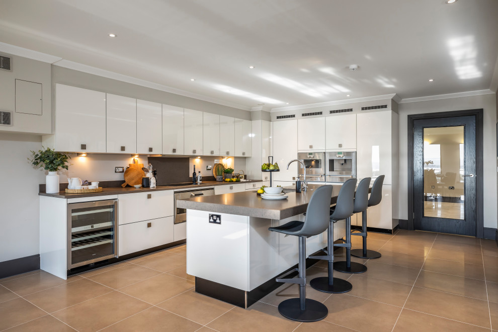 Photo of a contemporary l-shaped kitchen in Dorset with a submerged sink, flat-panel cabinets, white cabinets, grey splashback, stainless steel appliances, an island, brown floors and grey worktops.