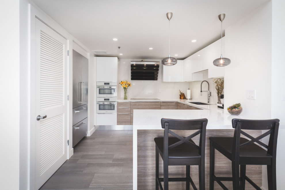 Photo of a small contemporary u-shaped eat-in kitchen in San Francisco with an undermount sink, flat-panel cabinets, white cabinets, quartz benchtops, white splashback, white appliances, medium hardwood floors, a peninsula, grey floor and white benchtop.