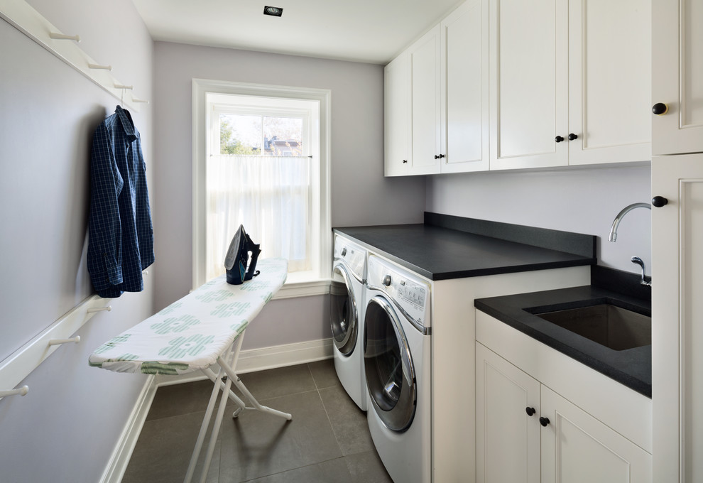 Transitional single-wall dedicated laundry room in New York with an undermount sink, white cabinets, grey walls, slate floors and a side-by-side washer and dryer.