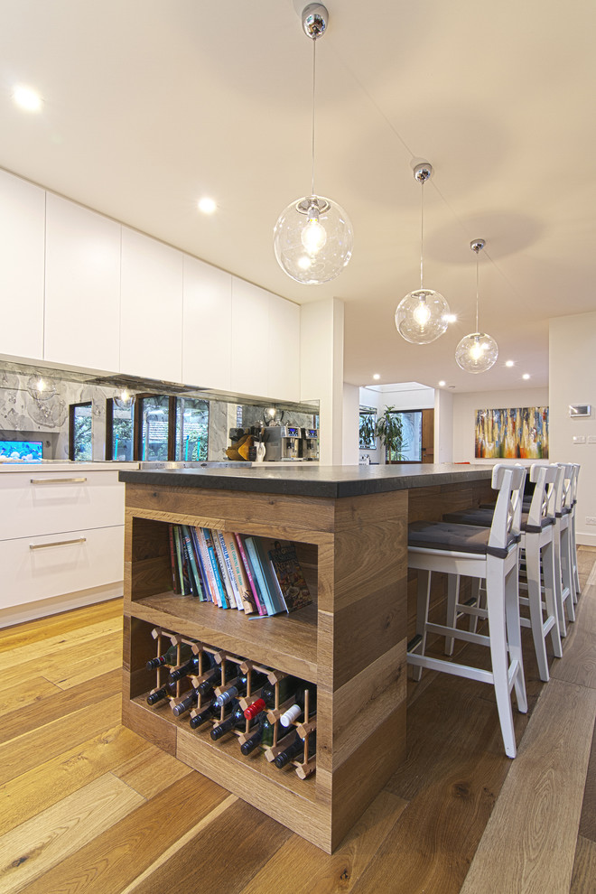 Inspiration for a large modern l-shaped eat-in kitchen in Melbourne with an undermount sink, flat-panel cabinets, white cabinets, quartz benchtops, metallic splashback, mirror splashback, stainless steel appliances, medium hardwood floors and with island.