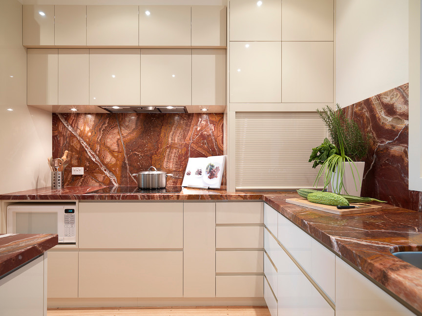 Photo of an expansive contemporary l-shaped eat-in kitchen in Melbourne with an undermount sink, flat-panel cabinets, white cabinets, onyx benchtops, multi-coloured splashback, stainless steel appliances, yellow walls, light hardwood floors and with island.