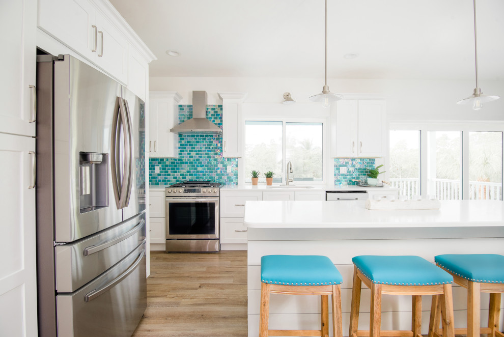 Inspiration for a mid-sized beach style l-shaped eat-in kitchen in Other with a single-bowl sink, shaker cabinets, white cabinets, quartz benchtops, blue splashback, glass tile splashback, stainless steel appliances, vinyl floors, with island, grey floor and white benchtop.