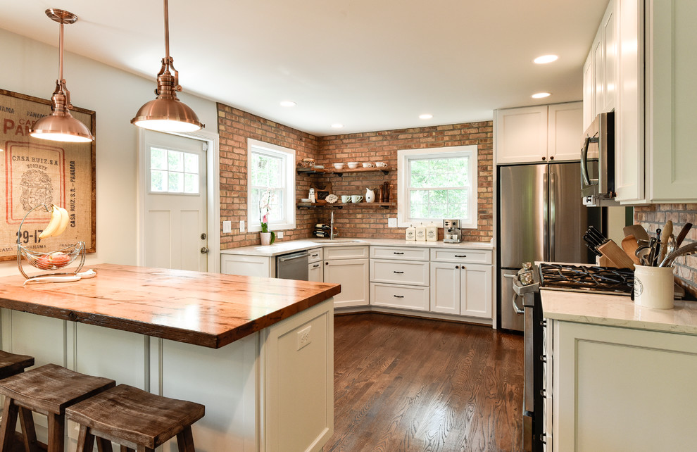 Photo of a mid-sized country u-shaped separate kitchen in DC Metro with an undermount sink, white cabinets, stainless steel appliances, shaker cabinets, wood benchtops, red splashback, brick splashback, dark hardwood floors, a peninsula and brown floor.