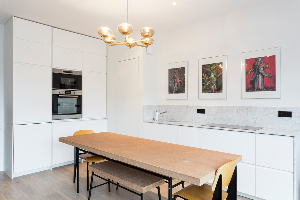 Photo of a mid-sized eclectic l-shaped eat-in kitchen in Paris with light hardwood floors, beige floor, an undermount sink, flat-panel cabinets, white cabinets, marble benchtops, white splashback, marble splashback, stainless steel appliances, no island and white benchtop.