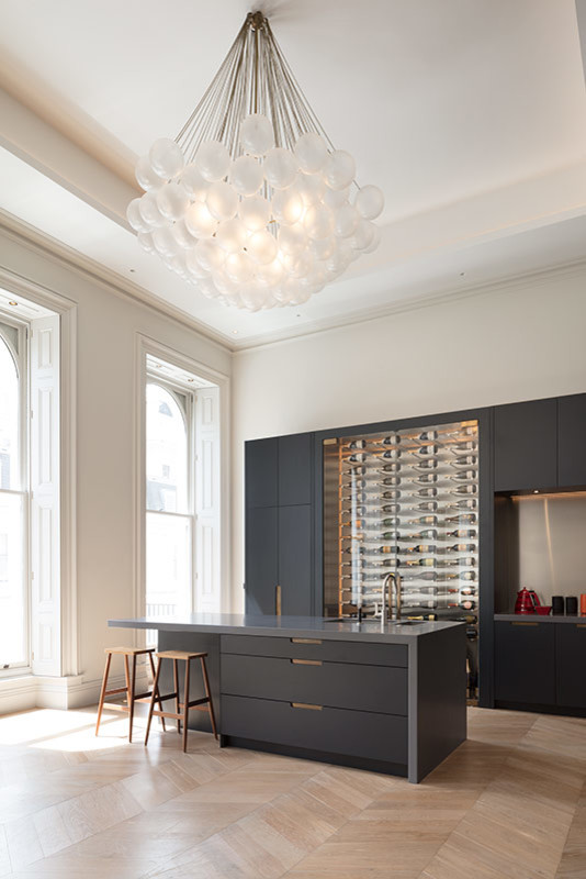 Inspiration for an expansive contemporary galley open plan kitchen in London with an undermount sink, glass-front cabinets, grey cabinets, solid surface benchtops, light hardwood floors, with island, brown floor and grey benchtop.