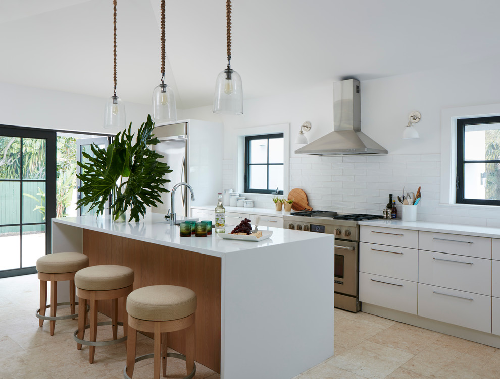 Inspiration for a beach style kitchen in Miami with flat-panel cabinets, white cabinets, white splashback, subway tile splashback, stainless steel appliances and with island.