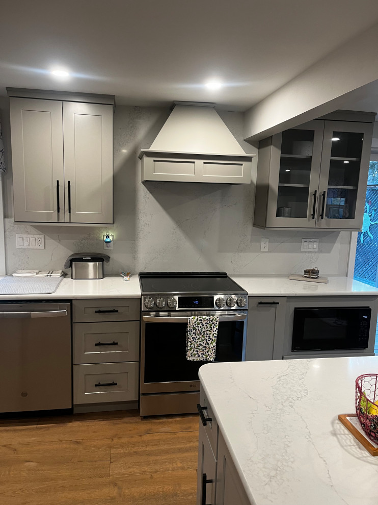 Inspiration for a mid-sized transitional u-shaped light wood floor and brown floor enclosed kitchen remodel in Boston with an undermount sink, shaker cabinets, gray cabinets, quartz countertops, white backsplash, quartz backsplash, stainless steel appliances, a peninsula and white countertops