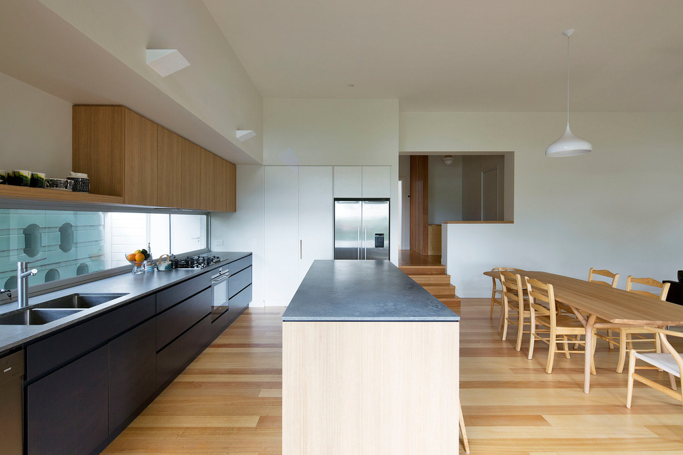 Inspiration for a mid-sized contemporary galley open plan kitchen in Sydney with an undermount sink, flat-panel cabinets, grey cabinets, quartz benchtops, glass sheet splashback, stainless steel appliances, medium hardwood floors, with island, brown floor and grey benchtop.