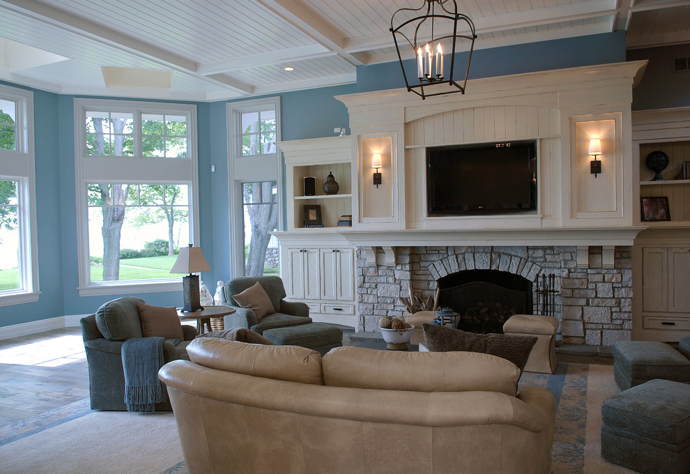 This is an example of an expansive beach style living room in Chicago with blue walls, medium hardwood floors, a standard fireplace, a stone fireplace surround, a built-in media wall, brown floor and vaulted.