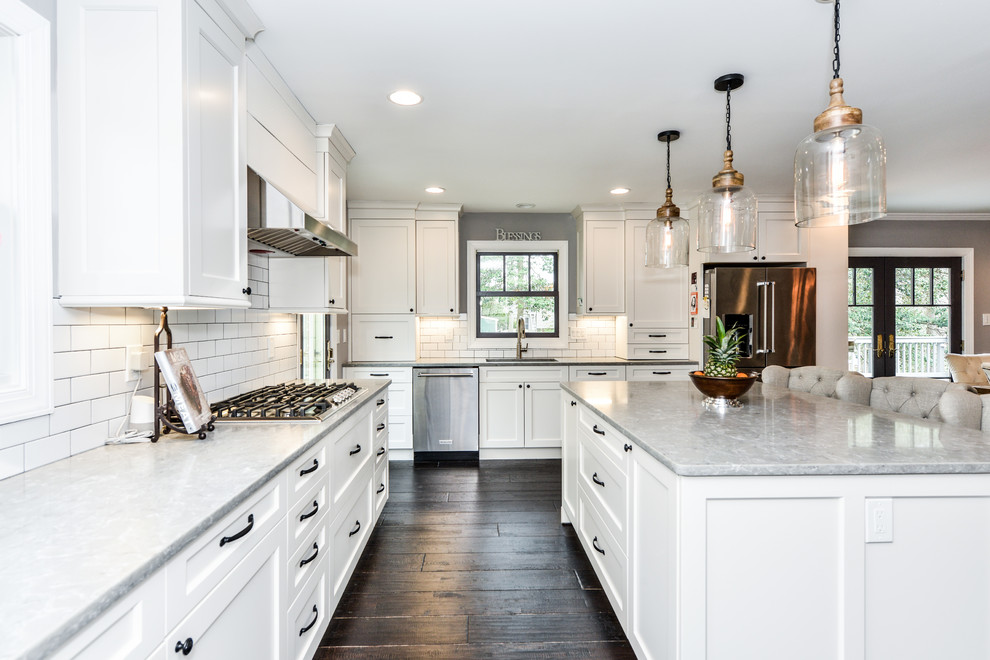 Design ideas for a transitional l-shaped eat-in kitchen in DC Metro with a drop-in sink, recessed-panel cabinets, white cabinets, quartz benchtops, white splashback, subway tile splashback, stainless steel appliances, dark hardwood floors, with island, brown floor and grey benchtop.