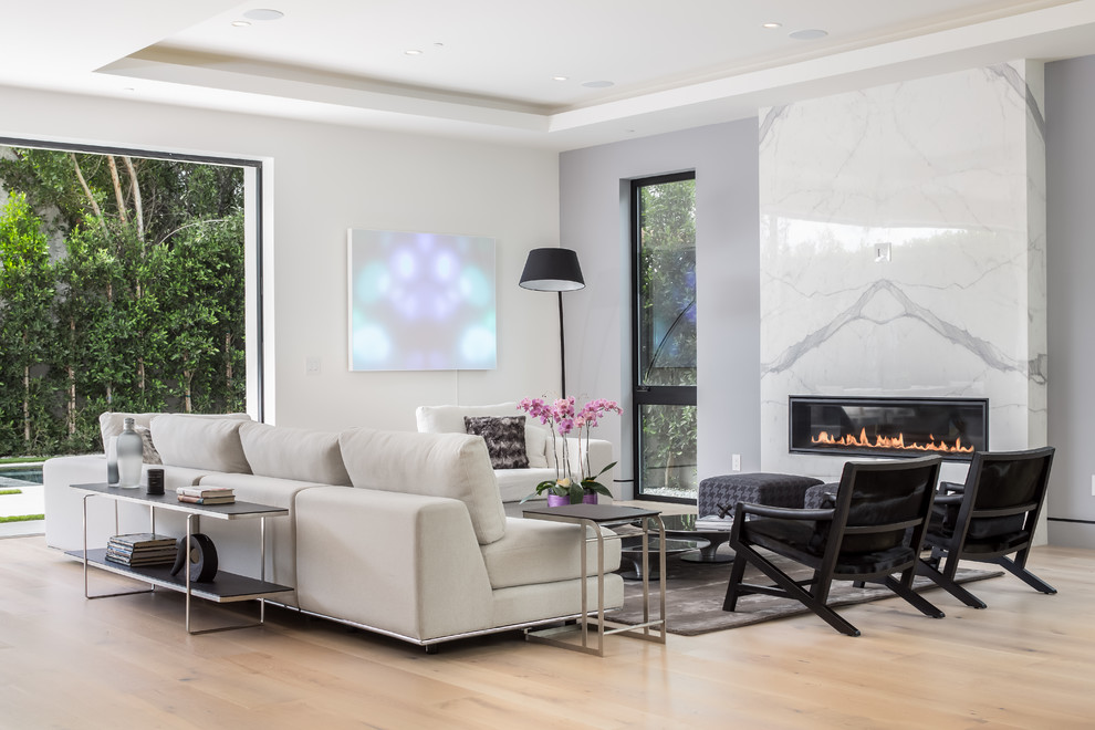 Contemporary open concept living room in Los Angeles with grey walls, light hardwood floors, a ribbon fireplace, a stone fireplace surround and beige floor.