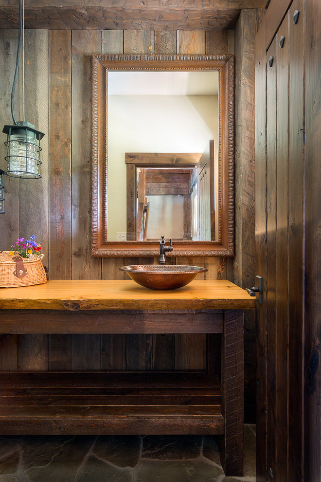 This is an example of a mid-sized country powder room in Jackson with furniture-like cabinets, brown cabinets, a two-piece toilet, brown tile, brown walls, slate floors, wood benchtops, green floor, orange benchtops and a vessel sink.