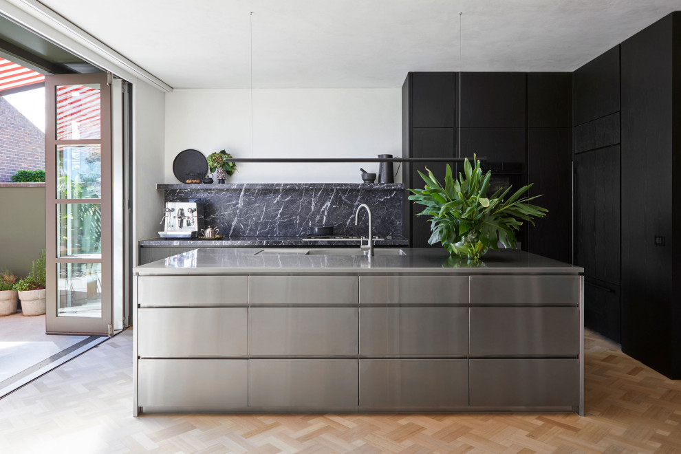 Contemporary l-shaped kitchen in Melbourne with flat-panel cabinets, black cabinets, grey splashback, stone slab splashback, black appliances, light hardwood floors, with island, beige floor and grey benchtop.