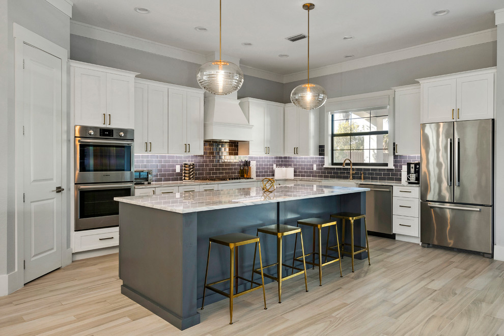 Large transitional l-shaped kitchen in Orlando with a farmhouse sink, white cabinets, marble benchtops, stainless steel appliances, with island, shaker cabinets, subway tile splashback, beige floor and grey benchtop.
