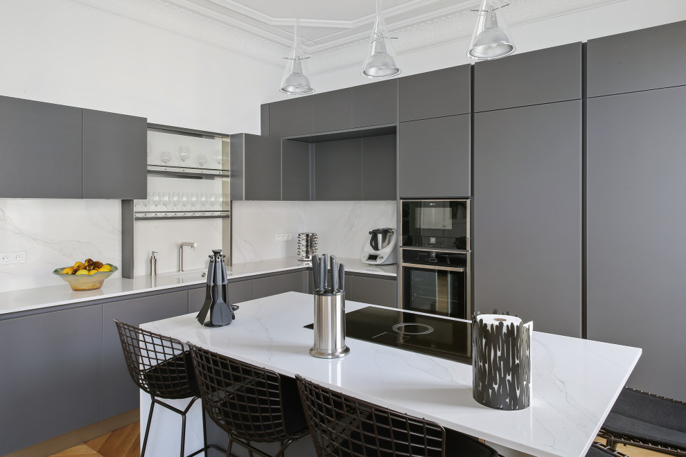 パリにあるラグジュアリーな広いコンテンポラリースタイルのおしゃれなアイランドキッチン (インセット扉のキャビネット、グレーのキャビネット、白いキッチンパネル、アンダーカウンターシンク、黒い調理設備) の写真