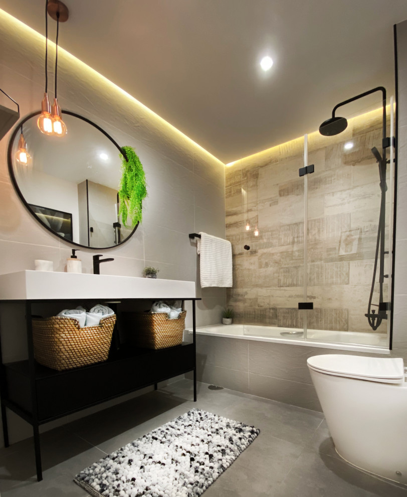 Inredning av ett modernt litet badrum med dusch, med vita skåp, ett badkar i en alkov, en vägghängd toalettstol, grå kakel, klinkergolv i porslin, ett avlångt handfat och grått golv