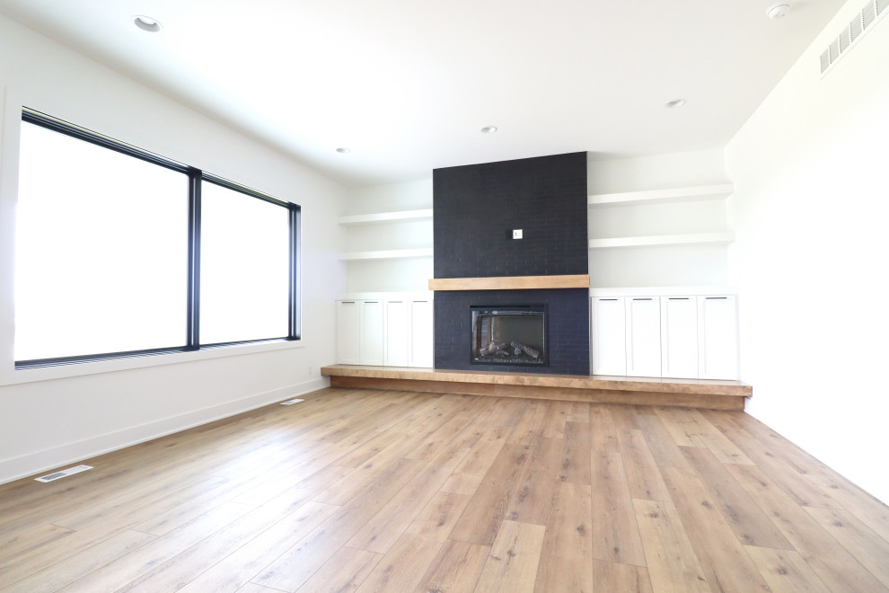 This is an example of a farmhouse open plan living room in Omaha with white walls, a standard fireplace, a brick fireplace surround and a wall mounted tv.